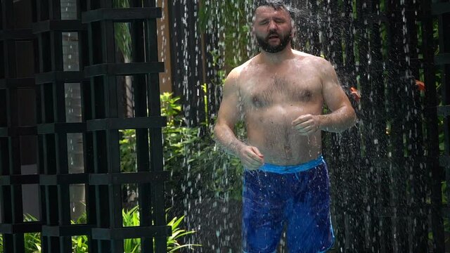 Man walking under shower by swimming pool, slow motion