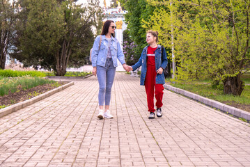 Mother and teenage daughter walking in a park, holding hands, happy young caucasian woman with long hair and teenage girl hanging out in a city, lifestyle family