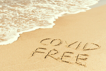 Covid free written on the shore, on the sand of a beach with wave washing the word, erasing or canceling it during Coronavirus summer, Covid free, safe beach, vaccine. Covid-19 immunity passport, pass