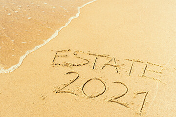 Estate 2021 written on the sand of a beach with wave washing, erasing or canceling it during Coronavirus summer, Covid free, safe beach, vaccine. Covid-19 immunity passport or pass, bathing season