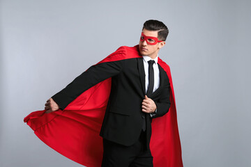Obraz na płótnie Canvas Businessman wearing superhero cape and mask on grey background