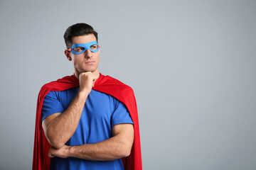 Man wearing superhero cape and mask on grey background. Space for text