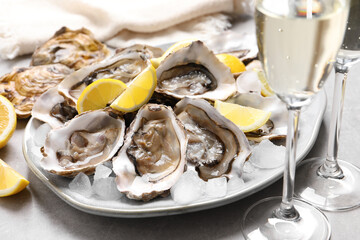Fresh oysters with lemon and glasses of champagne on grey table, closeup