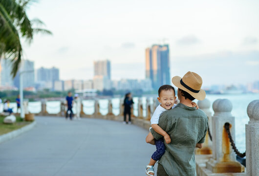Asian kid smiling in father's arm while walking along city beach together at Zhanjiang, Guangdong, China