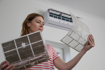 Woman replacing old dusty air filter with new one on air conditioner.