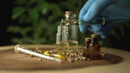 Fototapeta na wymiar Filling up glass jar bottle with cannabis cbd oil mixture for oral medical use. Made of green marijuana hemp plant on the background. Various organic medicine on the wood circle tree ring table.