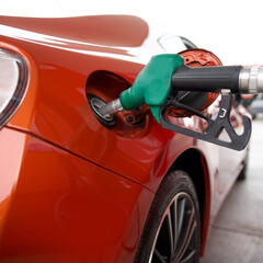 Green benzene gas pump nozzle filling up red sport car tank. Close up