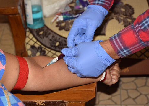 Indian Lab technician taking out blood for testing from a patient hand vein by injecting a syringe for medical examination for coronavirus. 