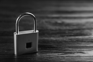Modern padlock on black wooden table. Space for text