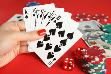 Woman holding playing cards with royal flush combination at red table, closeup