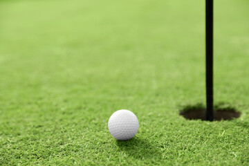 Golf ball near hole on green course, space for text