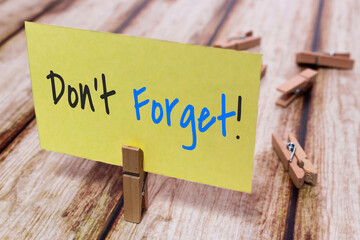 Conceptual message card showing Don't Forget on shabby wooden table. Nice wooden clothespin or natural wooden pinch holding yellow paper note. Reminder to keep memory or important schedule and event.