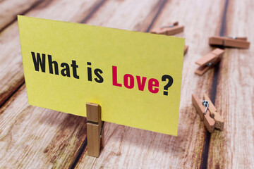 Conceptual message card showing What is Love? on shabby wooden table. Wooden clothespin or natural...