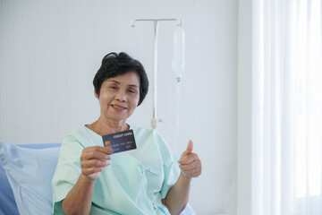 Selective focus on Asian senior patient woman holding blue credit card in her hand, smile and thumb...