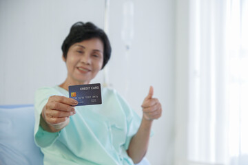 Selective focus on blue credit card that Asian senior patient woman holding in hand, smile and...