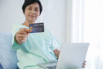 Selective focus on blue credit card that Asian senior patient woman holding in her hand and smile....