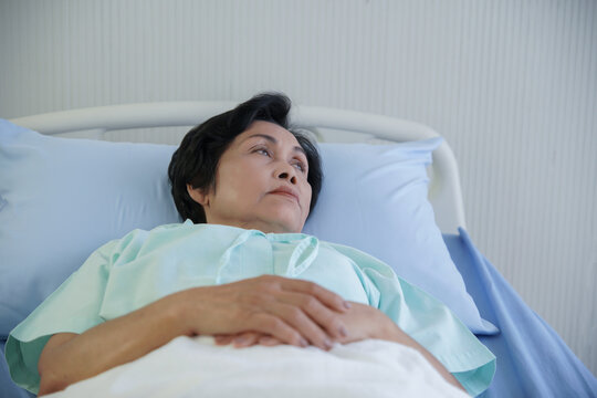 Asian elderly woman lying on bed with anxious and worried expression face. While she recuperating at hospital