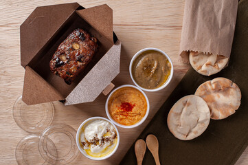 Fototapeta na wymiar Turkish kafta, accompanied by curd, hummus and babaganoush. Delivery packaging. Top view