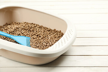 Cat litter tray with filler and scoop on white wooden floor, closeup