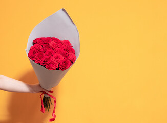 In your hand, hold a bouquet of red roses in a gray package. Yellow background with space for text. Selective focus.