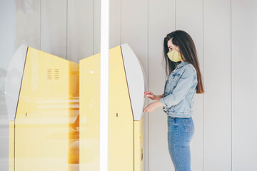 Woman with protective mask withdraws money from a bank card at an ATM.