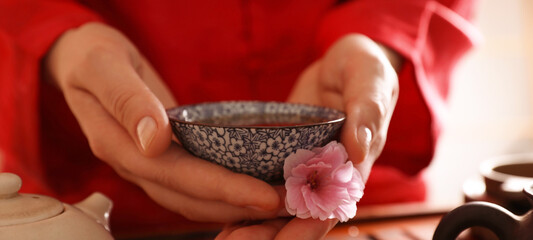 Guest holding cup of freshly brewed tea and sakura flower during traditional ceremony at table...