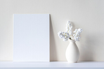 Soft light composition with blank canvas or sheet, vase, decorative house plant on a desk. White room interior, minimal mockup  with space for text
