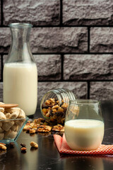 healthy breakfast or snack with milk bottle and glass of milk, cereals and nuts and chocolate on black marble counter and rustic wall
