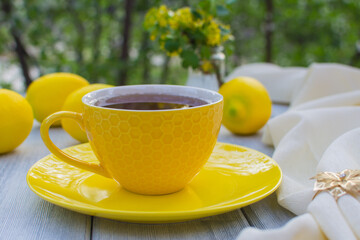 Yellow porcelain cup with tea with a yellow saucer on a wooden table. In the background are yellow lemons.
