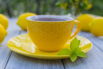 Yellow porcelain cup with tea with a yellow saucer on a wooden table. In the background are yellow lemons.