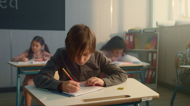 Schoolboy writing in notebook at lesson. Thoughtful boy holding pen at mouth