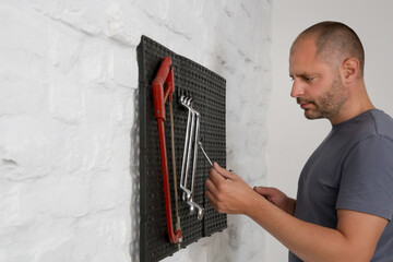Man organizing his tools on the plastic pegboard on the wall in workshop.