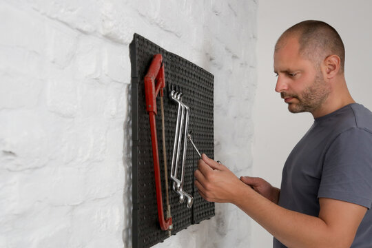 Man Organizing His Tools On The Plastic Pegboard On The Wall In Workshop.