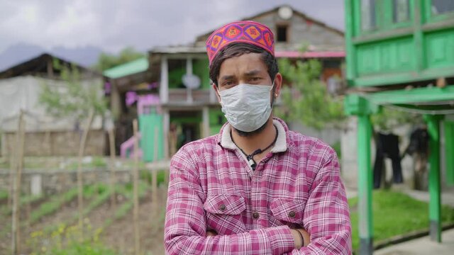 A of a young Indian male Himachali man (Pahari male) with protective face mask with the village houses in the background looking at camera in a broad daylight amid covid 19 epidemic