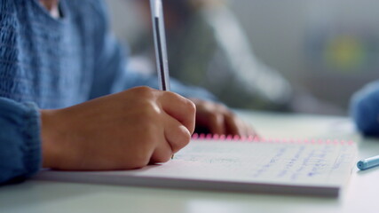 Schoolgirl hand doing class work at desk. Girl writing in notebook