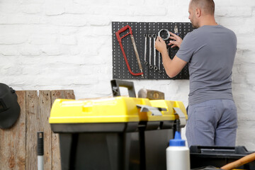 Man organizing his tools on the plastic pegboard on the wall in workshop. - obrazy, fototapety, plakaty