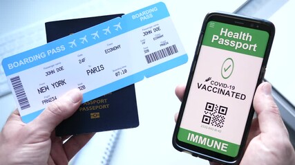 Holding a passport and plane ticket boarding pass in a hand and in the other a smartphone with a health passport with the Covid-19 proof of vaccination. - Powered by Adobe