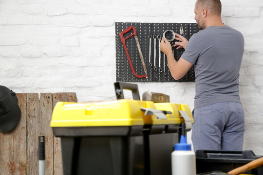 Man Organizing His Tools On The Plastic Pegboard On The Wall In Workshop.