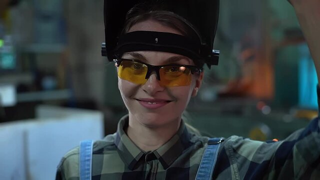 The female welder takes off her mask and smiles