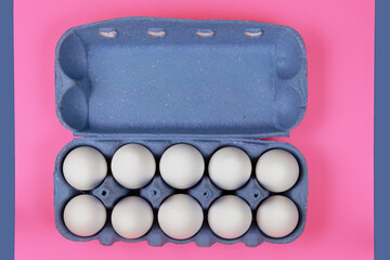 White chicken eggs in a paper tray on a pink surface