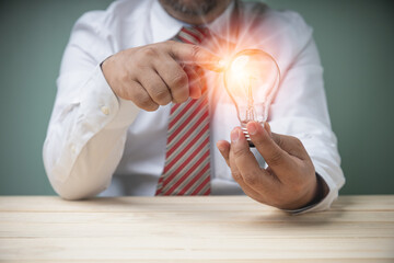 Businessman holding a light bulb on wooden desk in office with copy space. Creative new idea for development innovation, brainstorming for a solution. Technology, Inspiration, and innovation concepts.