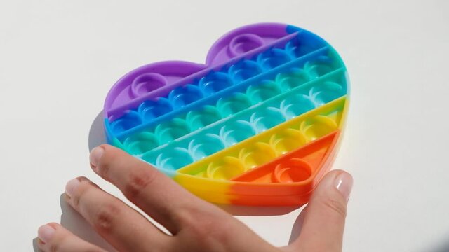 Hands play with antistress pop it toy. Rainbow sensory fidget isolated on white background. New trendy silicone toy.