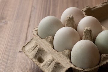 Picture of six egg in a paper box. The egg is white because they are duck egg not a chicken egg. They are organized in two rolls. The paper box is placed on the wooden table.
