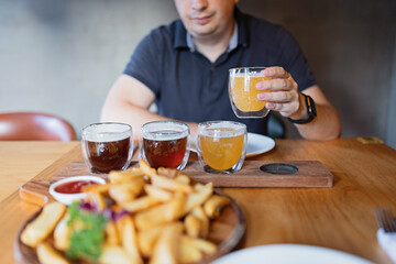 Man sampling variety of seasonal craft beer in pub. Beer samplers in small glasses individually placed in holes fashioned into unique wooden tray. Selective focus with shallow depth of field.