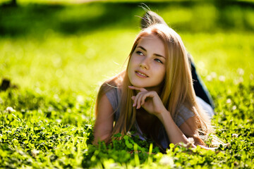 Naklejka na ściany i meble A beautiful girl lies in the park on the grass and dreamily looks around