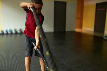 Strong fit Afro American boy exercising in gym using special tools for effective full-body workout....