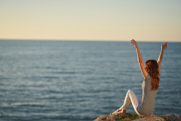 happy woman in a t-shirt and trousers by the sea raised her hands up