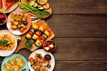 Vegan summer bbq or picnic side border. Above view over a dark wood background. Grilled fruit and vegetables, skewers, cauliflower steak and vegetarian sides. Copy space. Meat substitute concept.