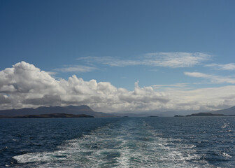 View from ferry to Outer Hebrides from The Minch sea with ferry water wake, distant views of mountains of Assynt and mainland Scotland. Sunny day, blue sky and cloud.