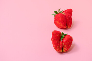 Two ugly strawberries on pastel pink background with copy space, selective focus. Deformed fruit concept